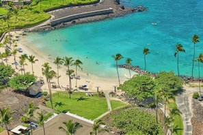 A coastal resort with a sandy beach, palm trees, and a clear blue sea.