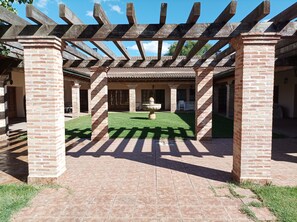 A covered outdoor area with brick pillars and a pergola, featuring a central fountain and a grassy lawn.