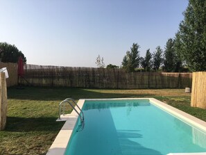 A rectangular swimming pool with a metal ladder, surrounded by a wooden fence and a grassy yard.