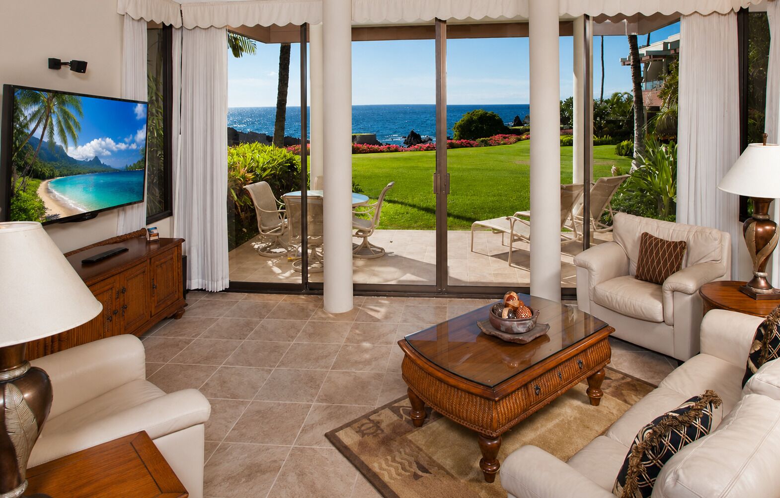 A living room with a large TV, comfortable seating, a coffee table, and a view of the ocean.
