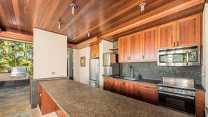 Une cuisine moderne dotée de plans de travail en granit, d’armoires en bois, d’appareils électroménagers en acier inoxydable et d’un pare-feu en pierre.