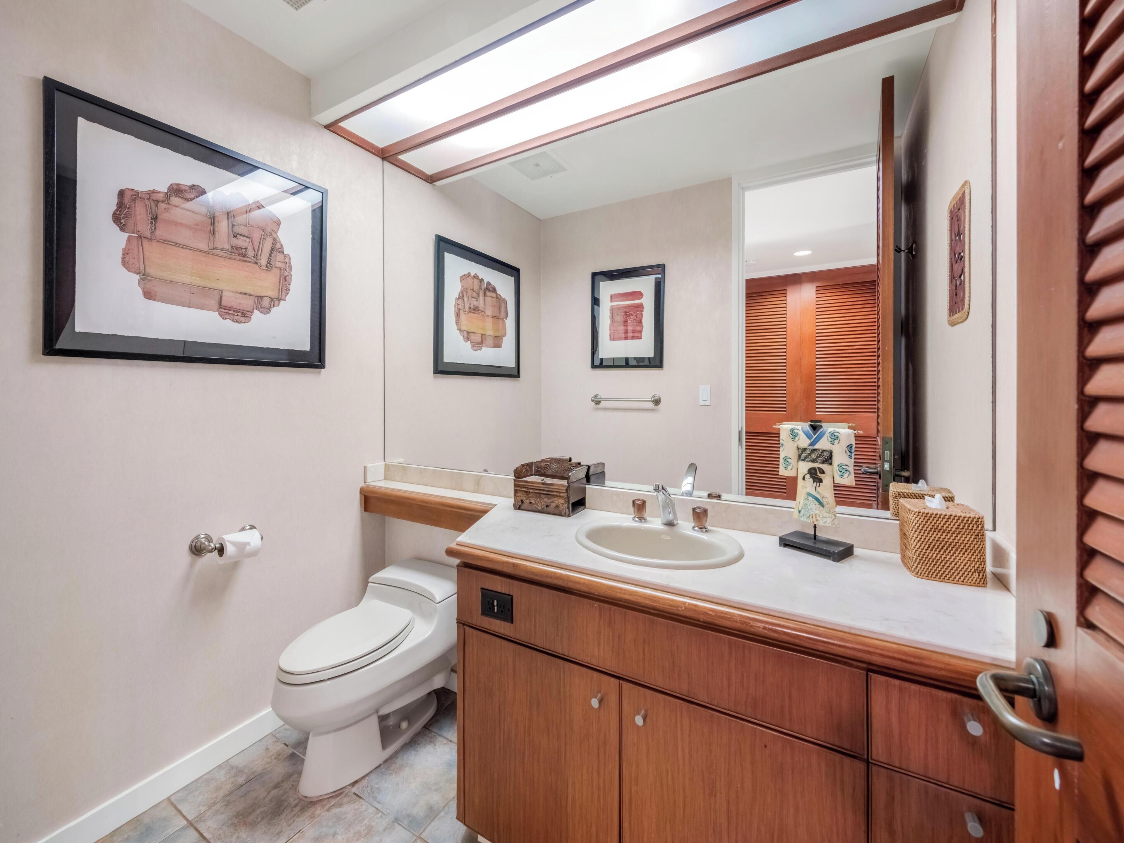 Une salle de bain avec des toilettes blanches, un meuble-lavabo en bois et des œuvres d’art encadrées accrochées au mur.