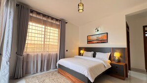 Une chambre à coucher avec un lit, des lampes de chevet, une table de nuit, une fenêtre avec des rideaux et un tableau au mur.
