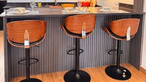 Een moderne keuken met een centraal kookeiland, drie houten barstoelen, hanglampen en houten kastjes.