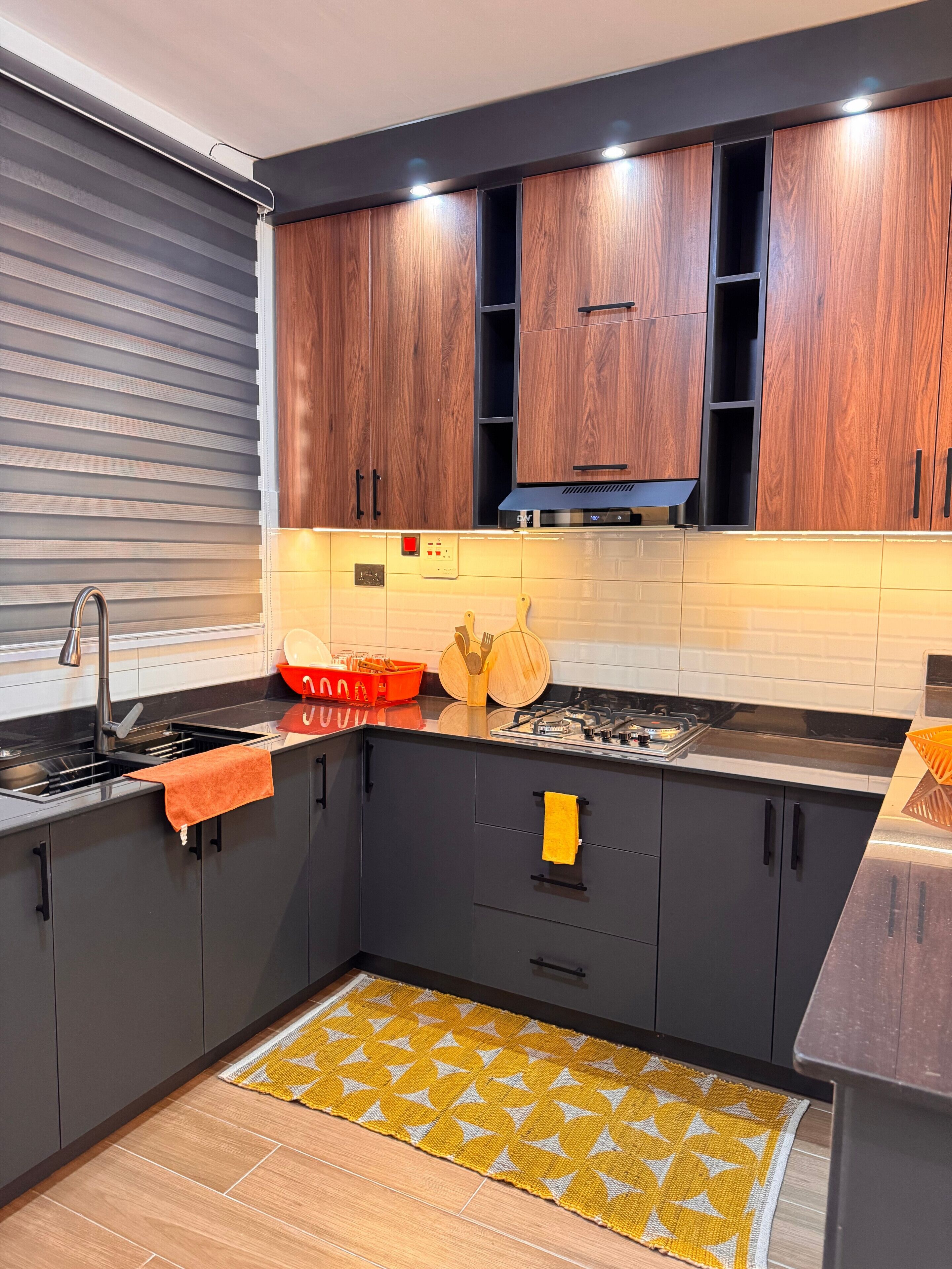 Una cucina moderna con mobili scuri, un lavandino in acciaio inossidabile e un tappeto giallo decorato.