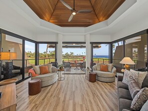 A spacious living area with a wooden ceiling, large windows offering a view of a golf course and ocean, and modern furniture.