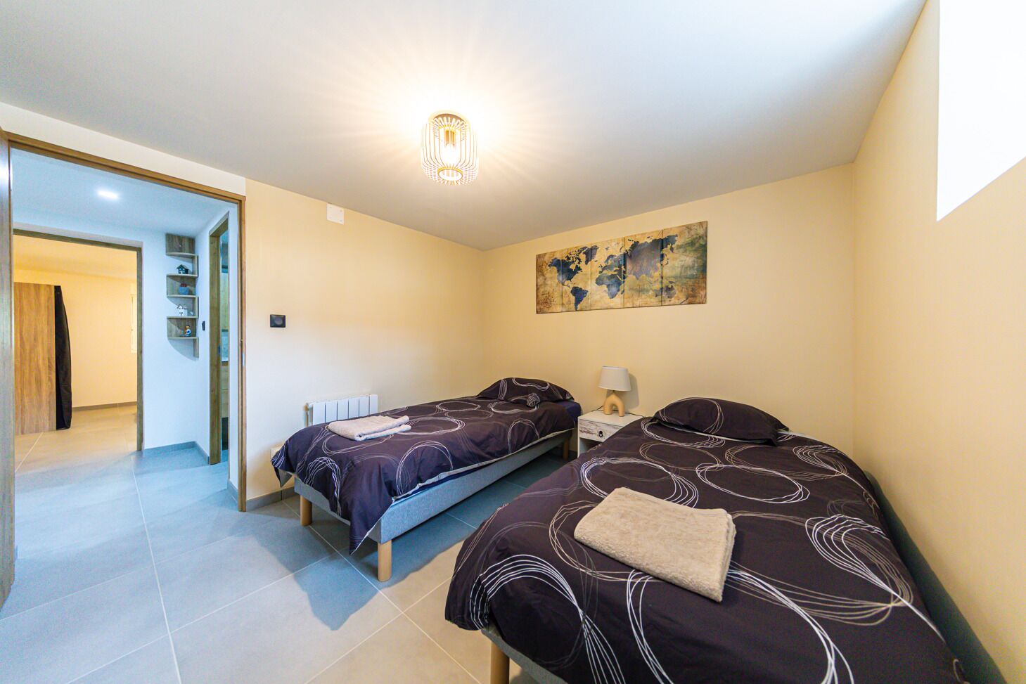 Ein Schlafzimmer mit zwei Betten, einer Weltkarte an der Wand, einer Heizung und einer Tür zu einem anderen Raum.