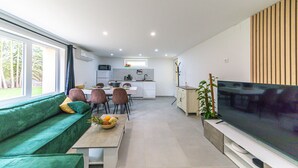 A modern living room with a green sofa, a dining area, a kitchen, and a TV. - Private 3-seater Jacuzzi, garden, air conditioning & parking - Dieulouard A31 (Dieulouard)