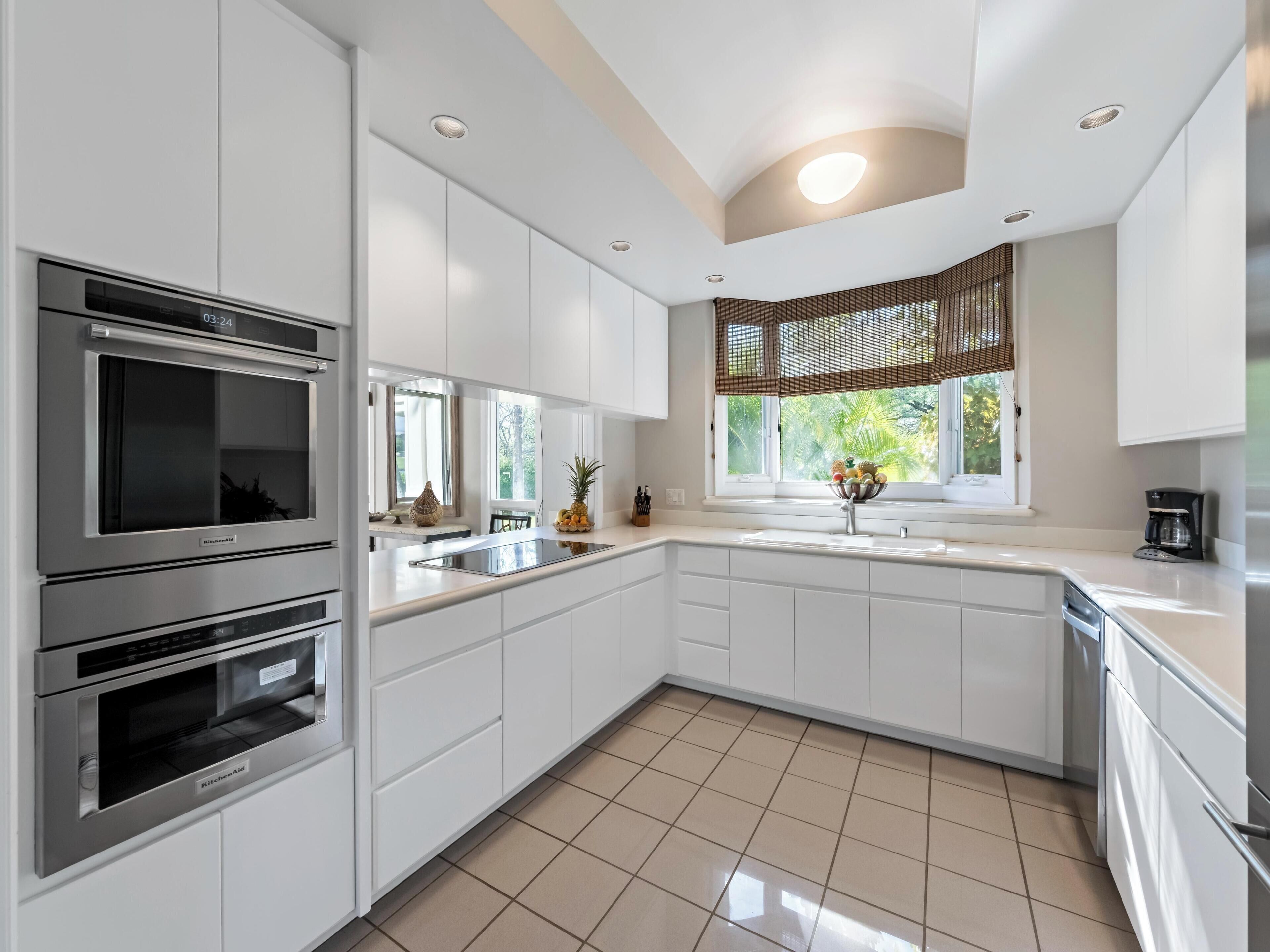 A modern kitchen with white cabinetry, a built-in oven, a microwave, and a window with a view of greenery.
