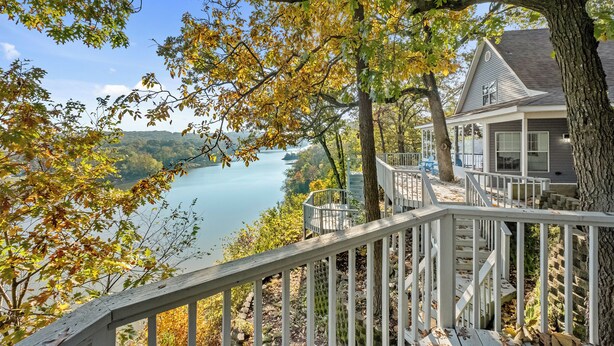 Une maison dotée d’une terrasse donnant sur un lac, entourée d’arbres aux feuilles d’automne.