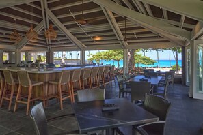 An outdoor seating area with tables and chairs, overlooking a beach with the ocean and a clear sky. - *CoralTree Managed* 3 Bedroom Private Home Close to Golf & Beaches - Kamilo 430 (Kamuela)