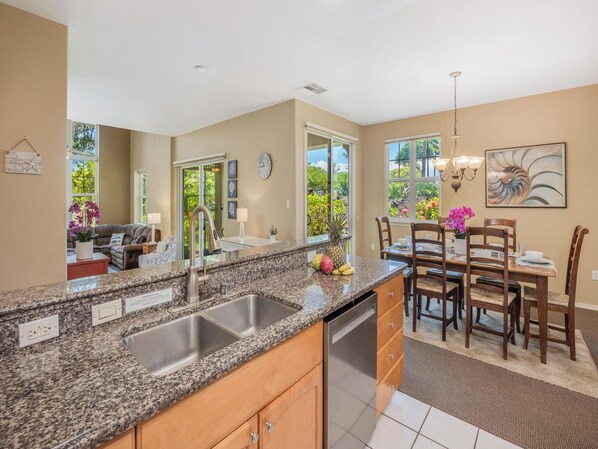 A modern kitchen with granite countertops, stainless steel appliances, and a dining area with wooden chairs and a chandelier.