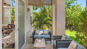 Un patio con mobiliario de mimbre, una mesa de madera y vistas a la vegetación y una palmera.