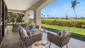 Un espace extérieur abrité, aménagé avec des meubles en osier, une table ronde et offrant une vue sur un terrain de golf.