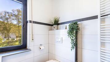 A bathroom with a toilet, a towel rack, a plant, and a window.