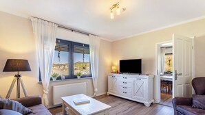 Un soggiorno moderno con un divano, un tavolino, una TV su un mobile bianco e una finestra con tende.