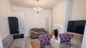 A compact living space with a sofa, two purple chairs, a glass-top dining table, a flat-screen TV, and a chandelier. - London Serenity House - 4 Bedrooms (London)