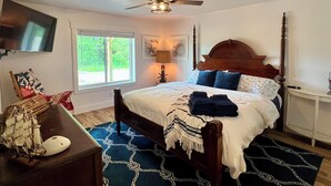 Une chambre à coucher avec un lit, un ventilateur de plafond, une fenêtre, un téléviseur et une maquette de bateau posée sur une table.