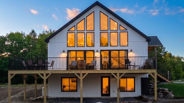 Une maison à deux étages dotée d’une terrasse, d’un foyer extérieur et de fauteuils Adirondack.