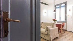 Una stanza con una porta, un divano beige, un tavolino e una finestra vista.