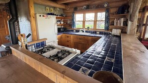 A rustic kitchen with a gas stove, wooden cabinets, and a blue-tiled backsplash. - Susie’s Place - Cozy Cabin (Bozeman)
