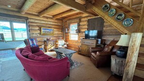 A log cabin interior with a red sofa, a wooden coffee table, a leather couch, and a television on a wooden cabinet. - Susie’s Place - Cozy Cabin (Bozeman)