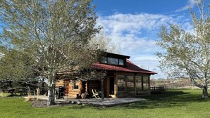 A rustic cabin with a red roof, large windows, and a covered porch area. - Susie’s Place - Cozy Cabin (Bozeman)