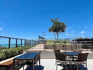 A rooftop patio with outdoor seating, a tree, and a view of the ocean.