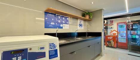 A modern hotel bathroom with a washing machine, sinks, and a Coca-Cola refrigerator.