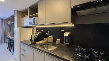 Una cocina moderna con estufa a gas, horno empotrado, cafetera y pileta.