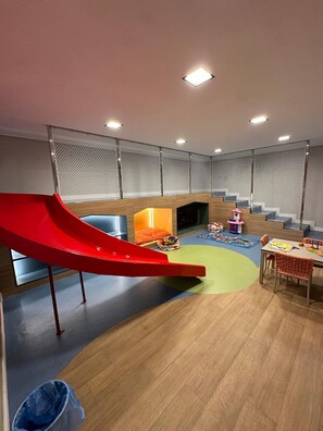 A children's play area with a red slide, a play mat, and a seating area with a table and chairs. - Move Tambau 108 (João Pessoa)