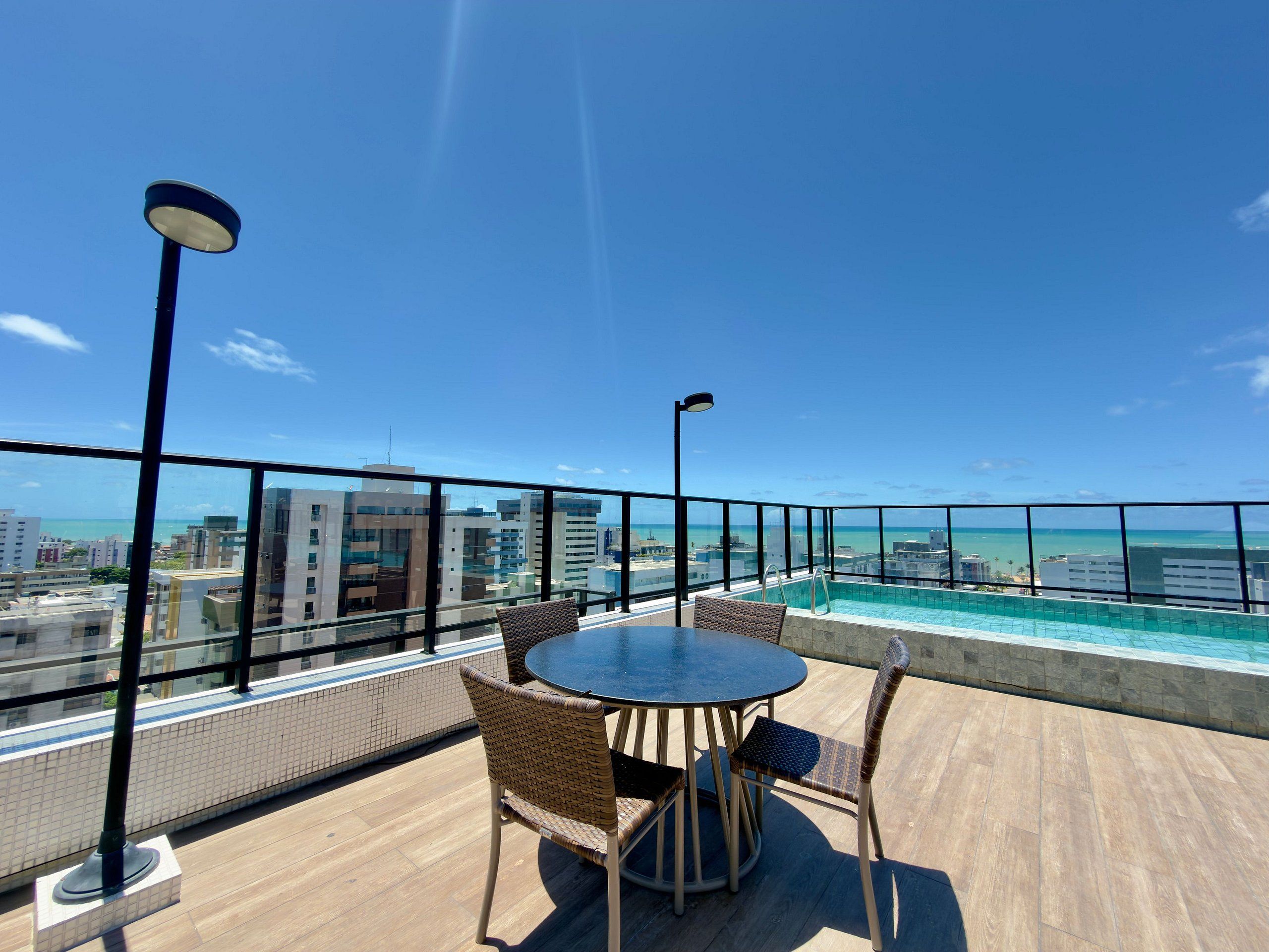 A rooftop terrace with a pool, outdoor seating, and a view of the city and ocean.