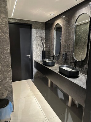 A modern bathroom with two sinks, a large mirror, and a door.