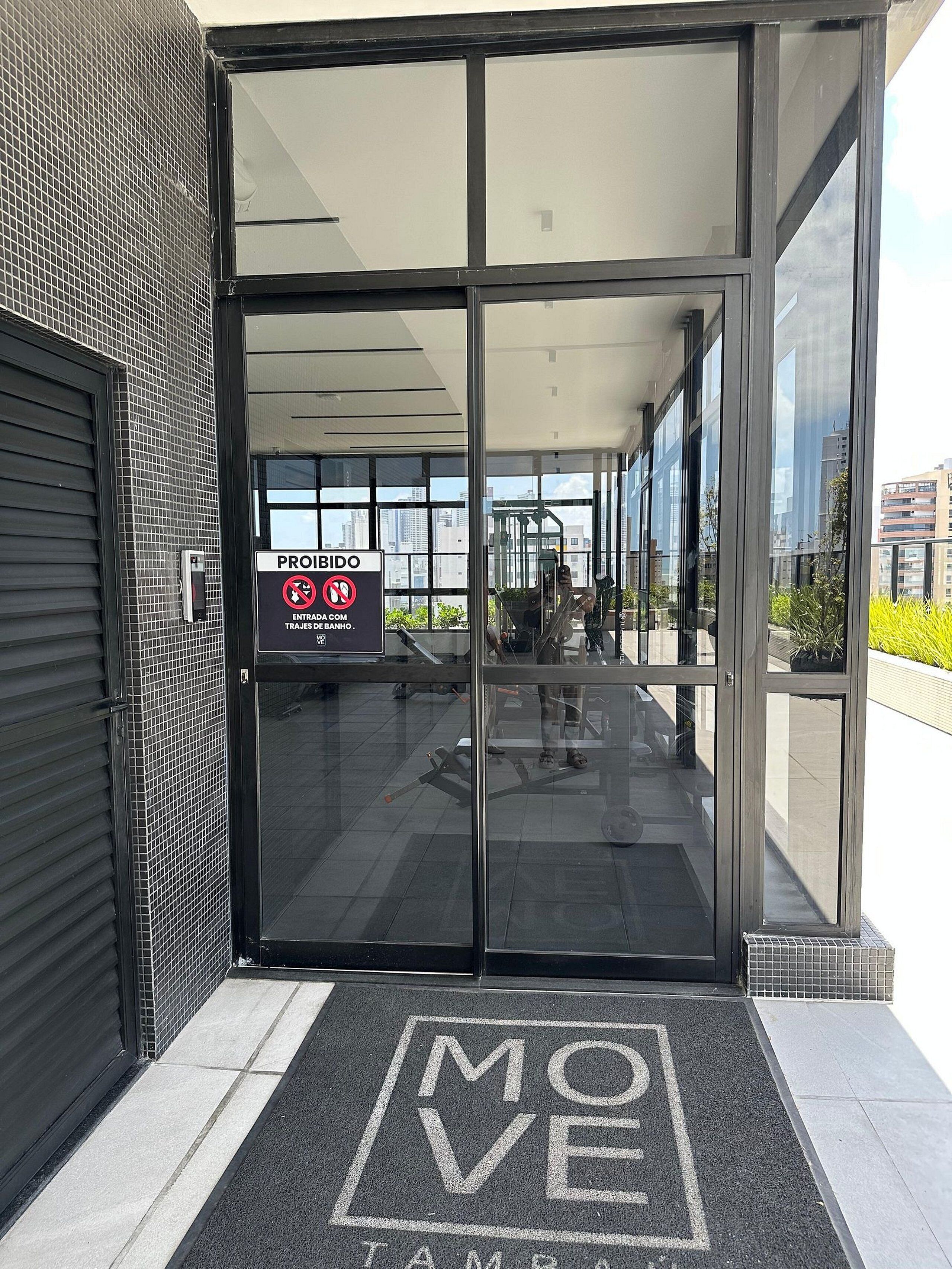 Entrada de un edificio moderno con puerta de vidrio, un cartel de 'PROHIBIDO' y un felpudo con la palabra 'MOVE'.