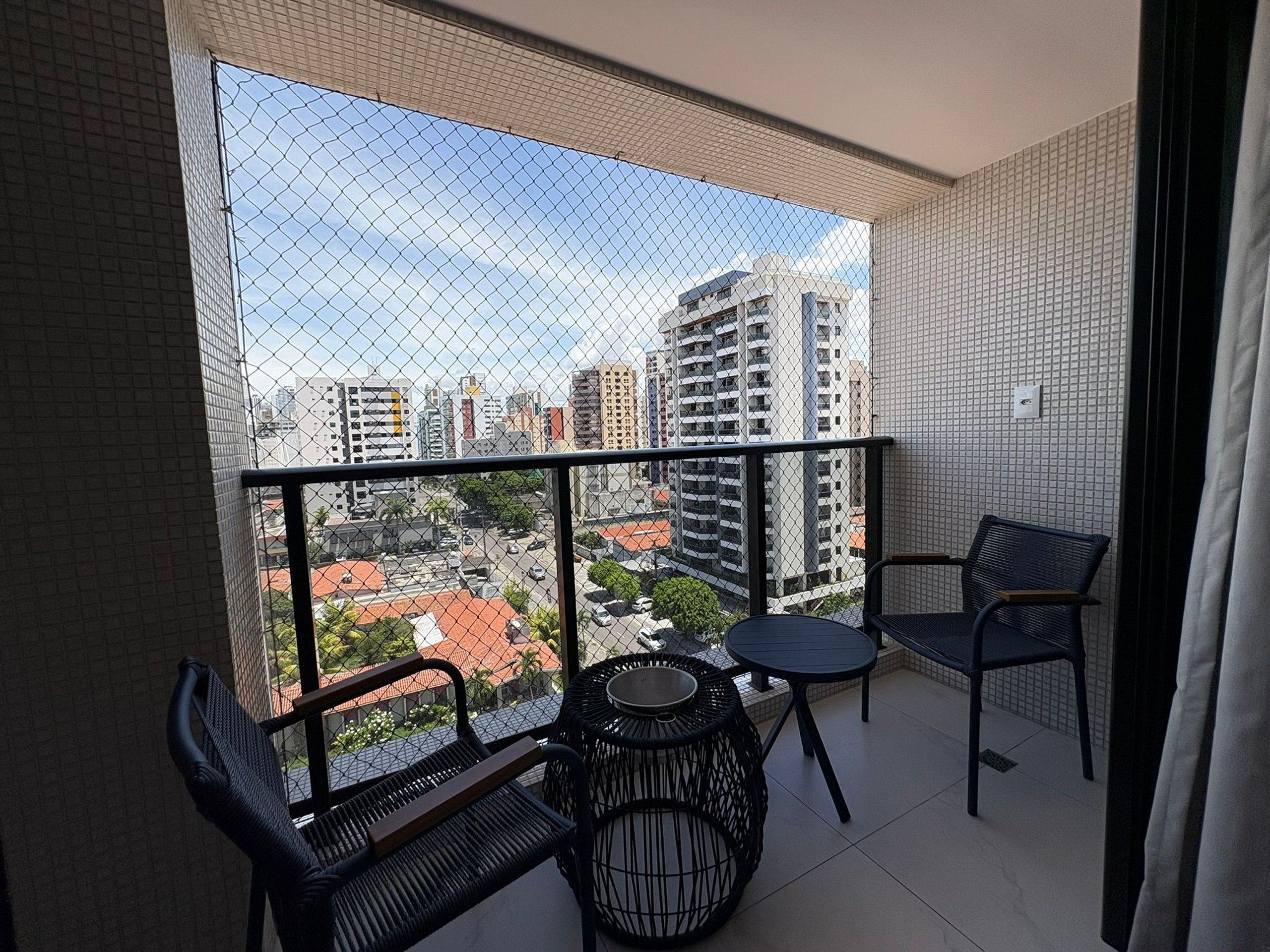 A balcony with a view of a cityscape, featuring a table and two chairs.