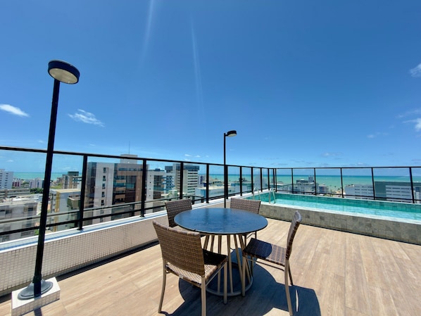 A rooftop terrace with a pool, outdoor seating, and a view of the city and ocean.