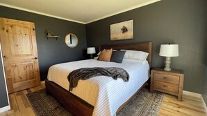 Une chambre à coucher avec un grand lit, deux tables de chevet, une porte en bois, un miroir et un tableau accroché au mur.