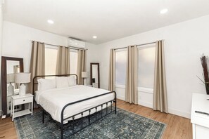 Une chambre à coucher avec un lit, des tables de chevet, un miroir, des rideaux et une fenêtre.