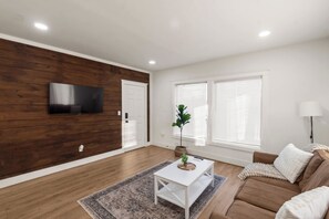 Un salon moderne avec un mur d’accent en bois, un téléviseur à écran plat, une table basse blanche, un canapé marron et une lampe.