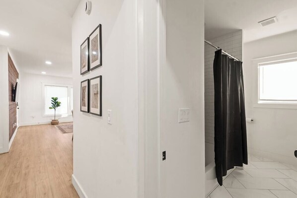 A hallway with a wooden floor leading to a bathroom with a shower curtain.