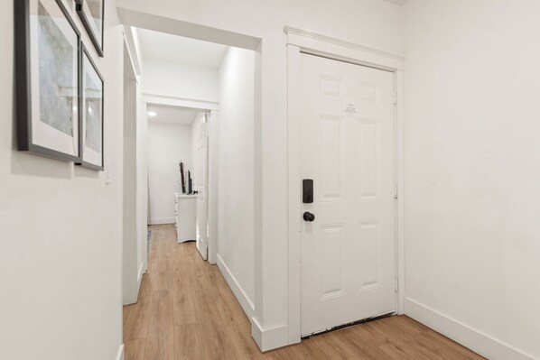 A hallway with a white door, a wooden floor, and a framed picture on the wall. - Modern EaDo Apt w/ Free Parking & Near Stadiums (Houston)