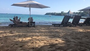 Una playa con sillas de descanso y sombrillas, un bote en el agua y una isla distante.
