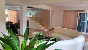 A spacious living area with a white sofa, a potted plant, and a staircase leading to an upper floor. - Villa Los Rios (Pedro Brand)