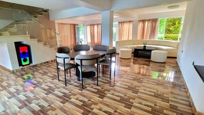 A spacious living area with a wooden floor, a dining table with chairs, a sofa, and a staircase. - Villa Los Rios (Pedro Brand)