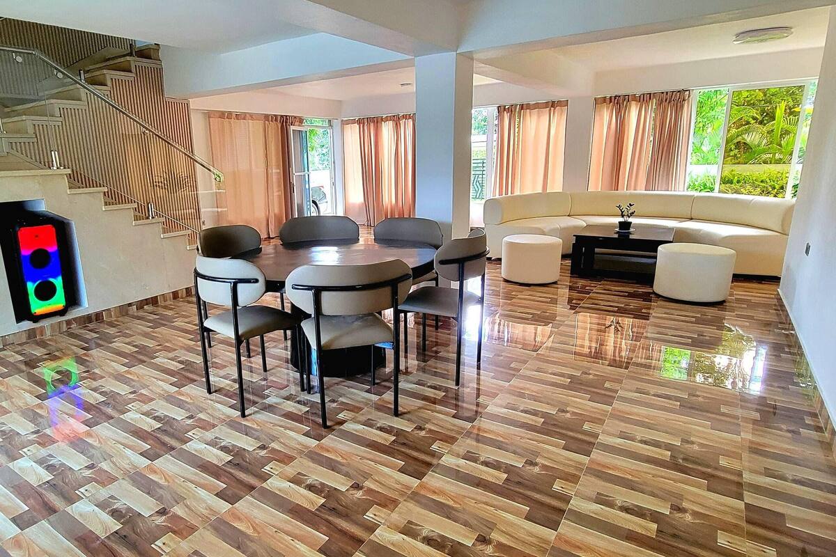 Amplia sala de estar con piso de madera, una mesa de comedor con sillas, un sofá y una escalera.
