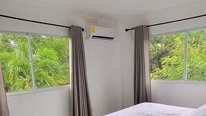 A bedroom with a bed, curtains, an air conditioning unit, and a window with a view of greenery. - Villa Los Rios (Pedro Brand)