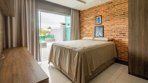 A modern bedroom with a large bed, a wooden desk, a brick accent wall, and a view through a glass door. - Blue House (Rio de Janeiro)