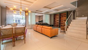 A modern living room with a sofa, dining table, and chairs. There is a staircase with a metal railing and a view of the outside. - Blue House (Rio de Janeiro)