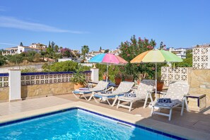 Ein Swimmingpool mit Liegestühlen und Sonnenschirmen, umgeben von einer Steinmauer und Topfpflanzen.