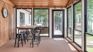 Una habitación amplia con techo de madera, ventanas grandes y una mesa larga con taburetes de bar.